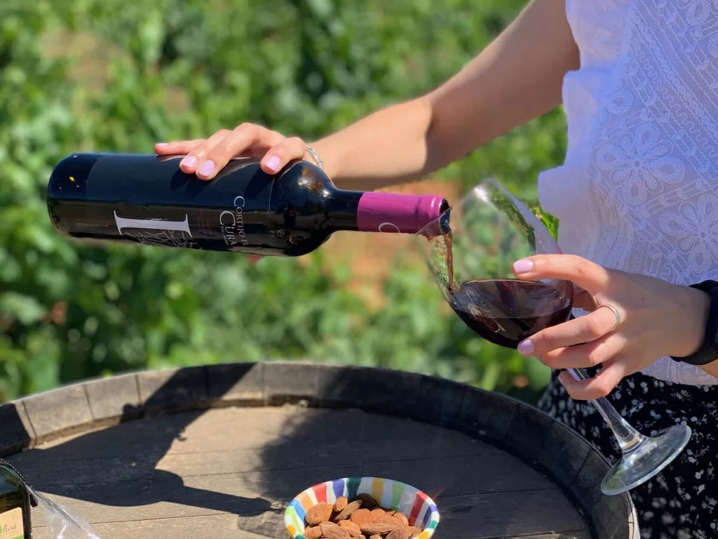 Mujer joven echando una copa de vino rosado joven Infante con un viñedo de fondo.